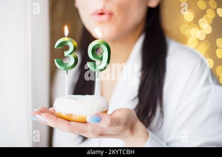 Eine Frau, die einen Kuchen mit den Kerzen Nummer 39 auf festlichem, verschwommenem Bokeh-Hintergrund hält. Stockfoto