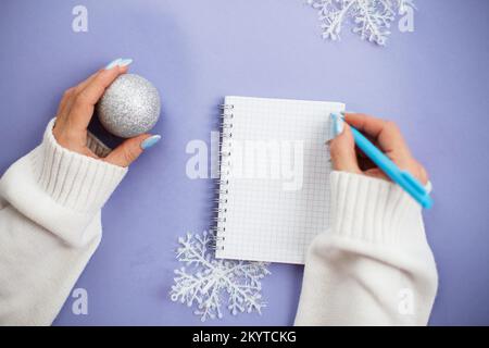 Frauenhand mit Winternägeln hält Stift auf Notizbuch und schreibt Wunschzettel. Stockfoto