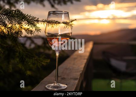 Champagner- und Cocktailgläser auf dem Glastisch auf der Außenterrasse mit Blick auf die Berge bei Sonnenuntergang Stockfoto