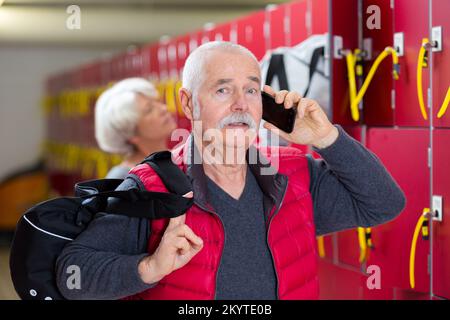 Ein erwachsener Mann, der in der Sportumkleide ein Smartphone benutzt Stockfoto