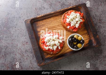 Griechische Dakos-Vorspeise mit Gerstenzwieback, Tomaten, Fetakäse, Oregano und Olivenöl auf dem Holzbrett auf dem Tisch. Horizontale Draufsicht von Stockfoto