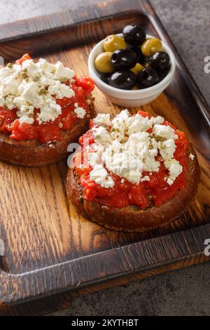 Traditionelles Meze oder eine leichte Mahlzeit auf der Insel Kreta, Dakos wird oft als griechische Bruschetta Nahaufnahme auf dem Holzbrett auf dem Tisch genannt. Vertikal Stockfoto