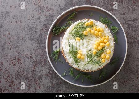 Klassischer Mimossalat mit Kartoffeln, Fischkonserven, Karotten, Eiern und Käse, gewürzt mit Mayonnaise, Nahaufnahme auf einem Teller auf dem Tisch. Horizontal oben vi Stockfoto