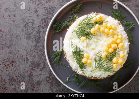 Mehrlagige Salat-Mimosa mit Gewürzkonserven, Kartoffeln, Käse, Karotten und Eiern auf dem Teller auf dem Tisch. Horizontale Draufsicht von oben Stockfoto