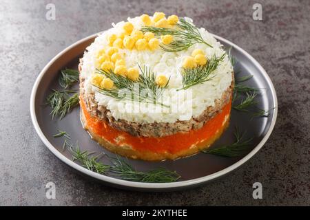 Klassischer Mimossalat mit Kartoffeln, Fischkonserven, Karotten, Eiern und Käse, gewürzt mit Mayonnaise, Nahaufnahme auf einem Teller auf dem Tisch. Horizontal Stockfoto