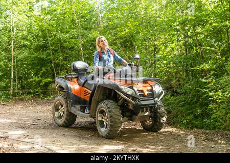 Lächelnde glückliche Frau, die an einem sonnigen Tag mit dem Quad fährt, gegen den blauen Himmel. Low-Angle-Aufnahme. Freiheit, Glück, Naturkonzept Stockfoto