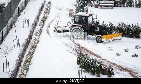 Traktor fegen Schnee mit rotierendem Pinsel und Schneepflug aus der Fußgängerzone auf der Brücke, Schneemanagement auf dem Bürgersteig bei Schneestürmen. Schneepflug entfernen Stockfoto