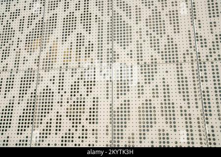 Beige Blechwand mit Löchern in Nahaufnahme. Fassade der Gebäudewand mit Metallblech mit ungleichmäßigen Lochgrößen und beige lackiert. Stockfoto