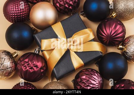 Geschenk in einer Schachtel und farbenfrohe Weihnachtsbälle auf hellem beigefarbenem Hintergrund. Draufsicht, flach liegend Stockfoto