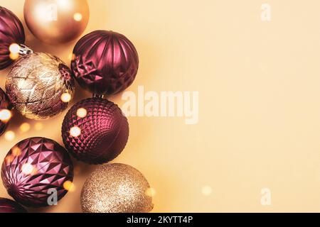 Goldene und lila glitzernde Weihnachtskugeln auf neutralem Hintergrund mit Kopierbereich. Draufsicht, flach liegend Stockfoto