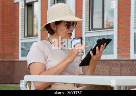 Frau benutzt einen Tablet-Computer und trinkt Kaffee im Straßencafé Stockfoto