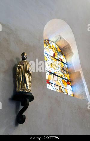 Religiöse Statue an einer Wand unter einem Buntglasfenster. Frankreich Stockfoto