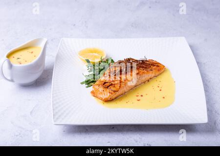 Lachs mit Beurre Blanc Sauce, Spinat und Zitrone. Garniert mit Lauch. Traditionelles französisches Gericht. Nahaufnahme. Stockfoto