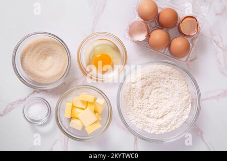 Draufsicht der grundlegenden rohen Backzutaten wie Eier, Zucker, Mehl, Butter, Salz, Auf einer Marmoroberfläche Stockfoto