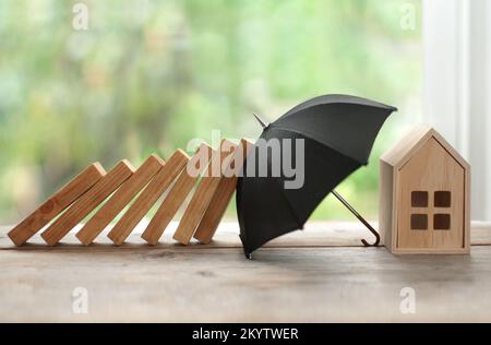 Regenschirm schützt Haus vor Dominoeinsturz, Versicherungskonzept Stockfoto