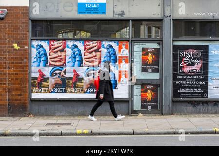 Ein Mann, der an einem geschlossenen Laden vorbeiläuft, mit Fenstern bedeckt, Plakate auf der Clerkenwell Road, London, Großbritannien. 20. November 2022 Stockfoto