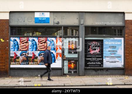 Ein Mann, der an einem geschlossenen Laden vorbeiläuft, mit Fenstern bedeckt, Plakate auf der Clerkenwell Road, London, Großbritannien. 20. November 2022 Stockfoto