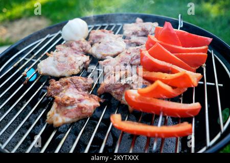 Schweinesteaks und rote Paprika, die draußen auf einem Holzkohlegrill gegrillt werden Stockfoto