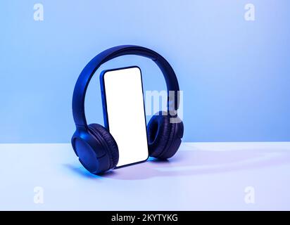 Smartphone mit bluetooth ® Kopfhörern mit weißem Bildschirm auf blauem Neonhintergrund, für Modell und Logo Stockfoto