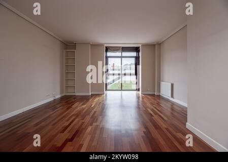 Leeres Wohnzimmer mit einem kleinen eingebauten Bücherregal, einem Pavillon mit Schiebefenstern und mahagonifarbenem Eichenboden Stockfoto