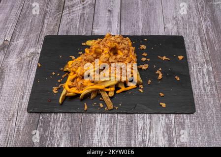 Ein Teller mit Pommes frites mit Haut, knusprigen Zwiebeln und Cheddar-Sauce Stockfoto