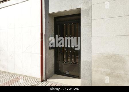 Kleine Metalltür zur Straße in einem freistehenden Gebäude mit grauer Granitfassade Stockfoto