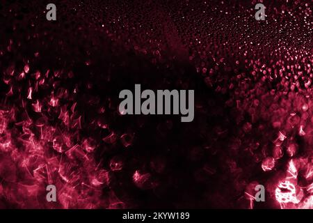 Viva Magenta Beleuchtung Wassertropfen Hintergrund. Wassertropfen auf einem Autoglas-Hintergrund. Wassertropfen auf Autoglas mit dunklem Bokeh-Hintergrund. Trendige Farbe 2023. Stockfoto