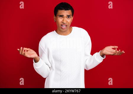 Foto eines jungen unzufriedenen Mannes Tragen Sie weißen Pullover Keine Ahnung Schultern zucken wie Probleme mit Weihnachtsgeschenken lösen isoliert auf rotem Hintergrund Stockfoto