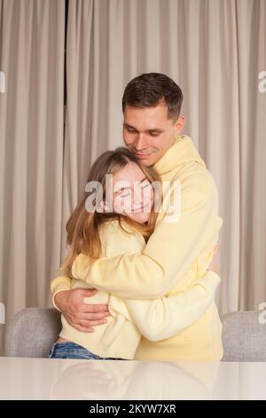 Lächelnder Mann und lächelnde Frau, Paar in gelben Kapuzen, umarmt und schaut sich vor dem Hintergrund des Studios an Stockfoto