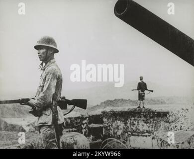 Ein altes Foto aus dem Jahr 1942 von japanischen Soldaten, die im Zweiten Weltkrieg mit Gewehren neben einer Küstenwaffenanlage bewacht wurden Stockfoto