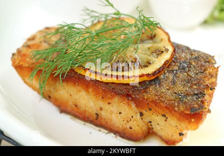 Nahaufnahme von köstlichem in der Pfanne gebratenem Wolfsbarsch mit Zitronenscheibe und Dill Stockfoto