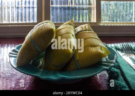 Goiânia, Goias, Brasilien – 01. Dezember 2022: 3 mit Maisschalen bedeckte Lamonas, auf einem Teller, vor einem Fenster und auf einer glänzenden Oberfläche. Stockfoto