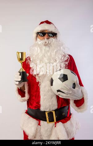 der weihnachtsmann mit Sonnenbrille, „Thug Life“-Fußball und einer Trophäe in der Hand auf weißem Hintergrund Stockfoto