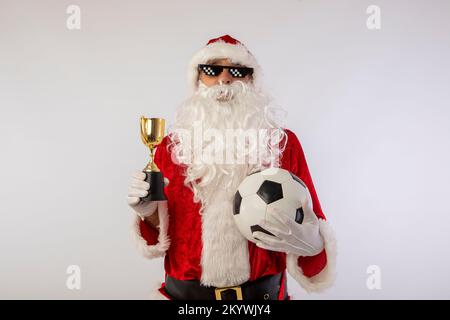 der weihnachtsmann mit Sonnenbrille, „Thug Life“-Fußball und einer Trophäe in der Hand auf weißem Hintergrund Stockfoto