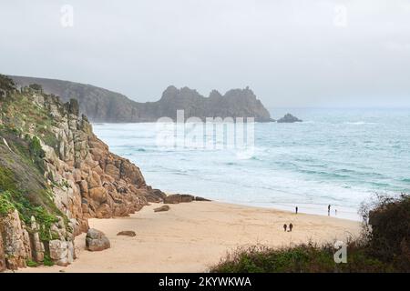 Urlauber am Strand von Porthcurno Bay, Cornwall, England, neben dem türkisfarbenen Wasser des Ozeans mit Blick auf Logan Rock. Stockfoto