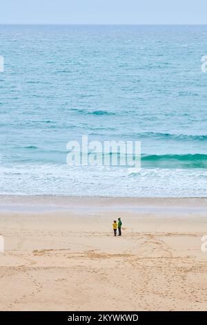 Ein Paar am Strand in Porthcurno Bay, Cornwall, England, neben dem türkisfarbenen Wasser des Ozeans. Stockfoto