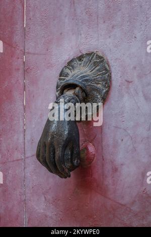 Großansicht des verwitterten alten Türklopfers aus Messing in Form einer Handkugel, isoliert an der himbeerroten Holztür, Montpellier, Frankreich Stockfoto