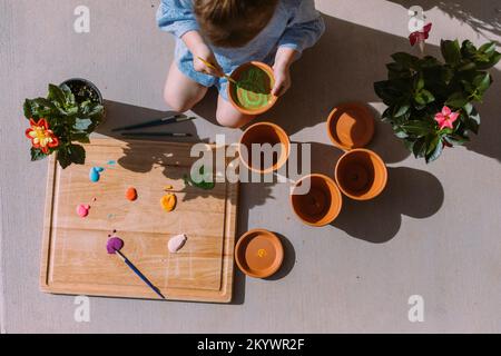 Ein kleines Mädchen malt Blumentöpfe draußen in der Sonne von Saint Geo Stockfoto