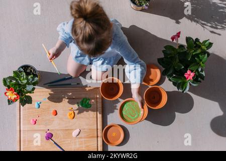 Ein kleines Mädchen malt Blumentöpfe draußen in der Sonne von Saint Geo Stockfoto