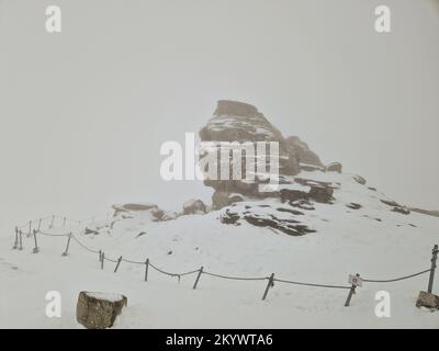 Die Sphinx (Sfinxul), eine natürliche Felsformation im Naturpark Bucegi im Bucegi-Gebirge Rumäniens, an einem verschneiten Wintertag. Stockfoto