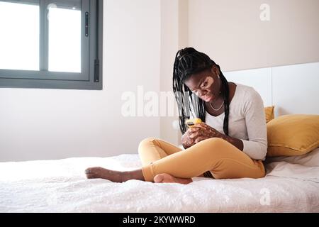 Schwarze Frau, die im Schlafzimmer ein Handy benutzt Stockfoto