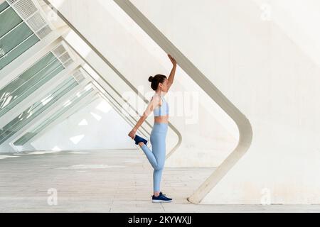 Sportliche Frau mit Beindehnung, Aufwärmübungen. Moderner urbaner Hintergrund. Stockfoto