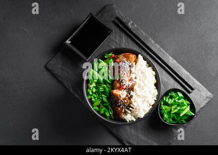 Asiatisches Essen. Thailändisches Essen. Reis mit Huhn und grünen Zwiebeln auf dunklem Hintergrund. Chinesisches Essen. Reis mit würzigem Kung pao-Huhn auf einem Teller. Horizontal Stockfoto