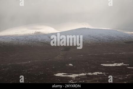 Wunderschöne Winterlandschaft von der Bergspitze in den schottischen Highlands hinunter in Richtung Rannoch Moor während Schneesturm und Spindrift von der Bergspitze hinein Stockfoto