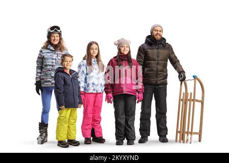 Junger Mann und Frau mit Kindern in Winterkleidung, die sich mit einem Holzschlitten auf weißem Hintergrund posieren Stockfoto