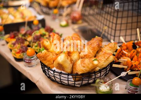 Korb mit Croissant-Sandwiches und leicht gesalzenem Lachsfilet auf dem Buffettisch Stockfoto