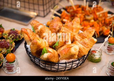 Korb mit Croissant-Sandwiches und leicht gesalzenem Lachsfilet auf dem Buffettisch Stockfoto