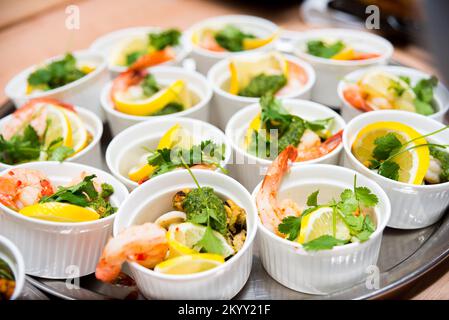 Viele Portionen Meeresfrüchte mit Zitrone in Ramekins, Garnelen, Muscheln und Tintenfischringen, garniert mit Koriander-Blättern Stockfoto