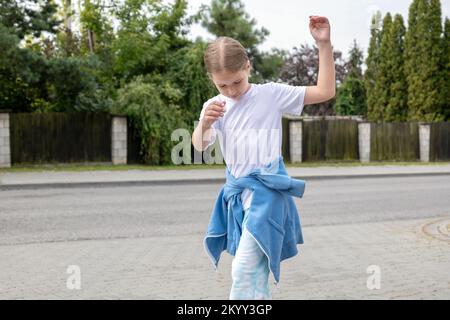 Glückliches Mädchen im Grundschulalter, Kind tanzt allein durch die Straße, Kopierraum, eine Person, verschwommener Hintergrund. Stressfreies Kinderglück Stockfoto