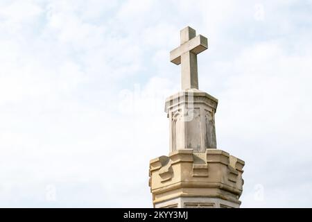 Altes Steinkreuz und hellblauer Himmel einfacher abstrakter Hintergrund, Kopierraum. Alter Friedhof Obelisk, Christentum, katholische Symbole, abstrakter Glaube Stockfoto